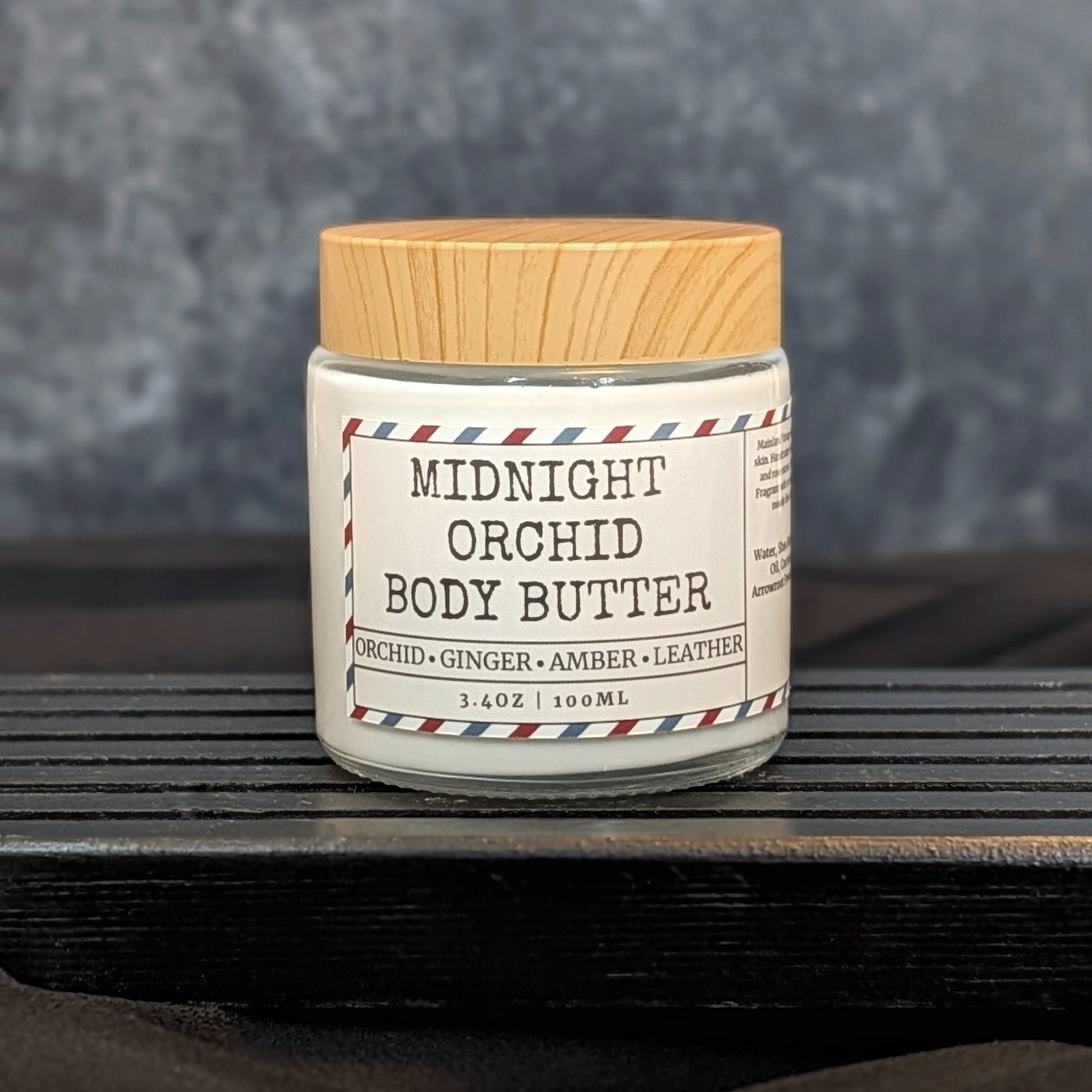 Jar of Midnight Orchid Body Butter on a wooden surface with a gray background