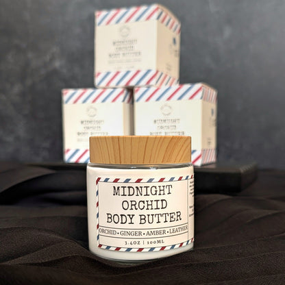 Jar of Midnight Orchid Body Butter with packaging in the background on a dark surface.