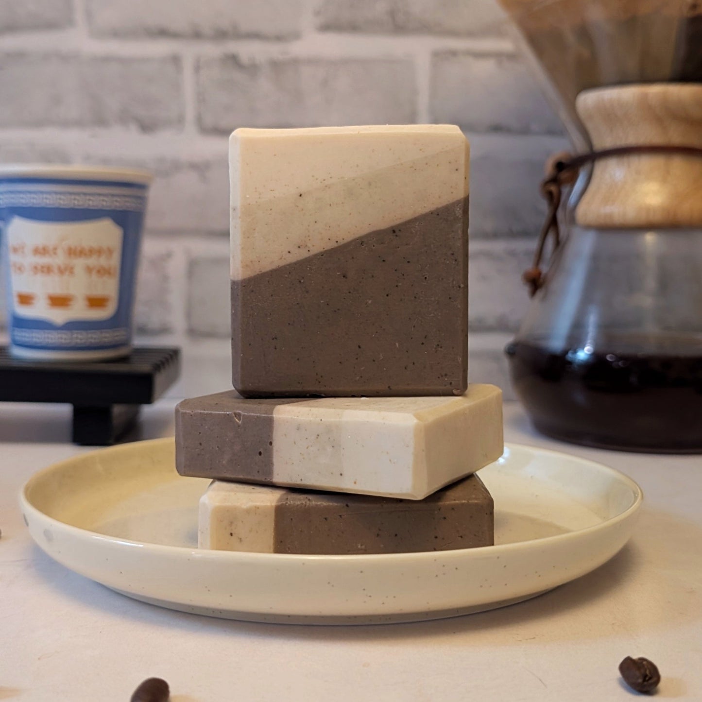 Stack of two-tone soap bars on a plate with coffee beans and a coffee maker in the background.