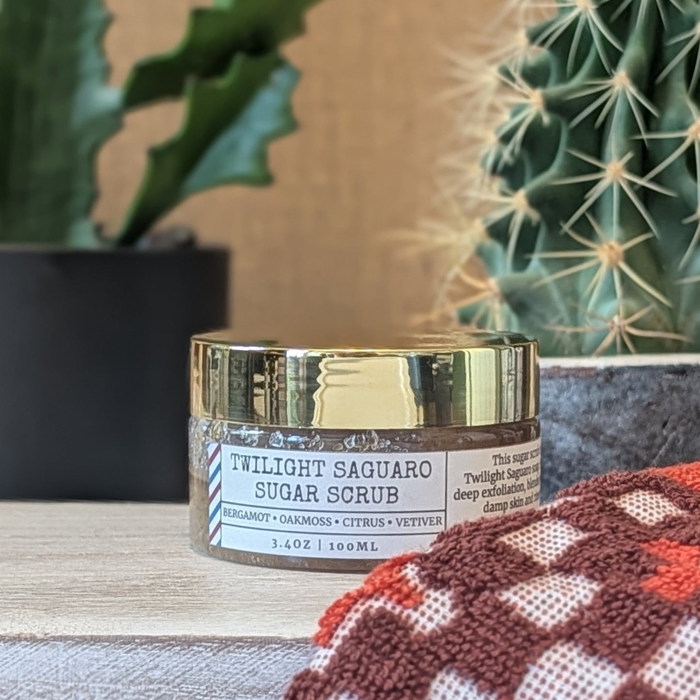 Twilight Saguaro Sugar Scrub jar with gold lid on a surface with plants in the background